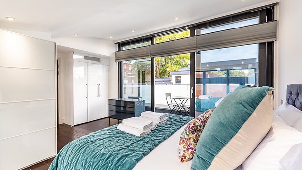 A modern bedroom with a large bed, a desk, and a view of the outdoors. - Tufnell Park retreat close to Hampstead Heath (London)