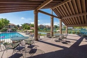 Un espace piscine extérieur doté d’un patio couvert, de chaises longues et offrant une vue sur le quartier environnant.