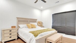 A bedroom with a bed, bedside tables, a bench, a ceiling fan, and a window with blinds. - Beautiful Victorville Home with all the amenities (Victorville)