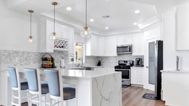 A modern kitchen with white cabinets, a marble island, and bar stools. - Beautiful Victorville Home with all the amenities (Victorville)