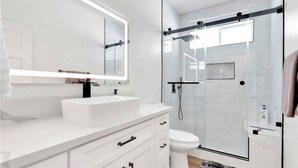A modern bathroom with a white vanity, a large mirror, a glass shower enclosure, and a toilet. - Beautiful Victorville Home with all the amenities (Victorville)