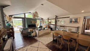 A spacious living area with a wooden floor, a sofa, a dining table with chairs, and a TV.