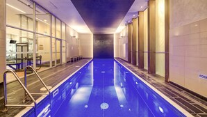 A long, narrow indoor swimming pool with clear lanes, surrounded by glass walls and wooden paneling, with a bench and a water fountain visible. - 3-bedroom apartment with Parking, Gym, Pool near Crown Casino & Eureka Tower (Southbank)