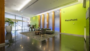 A modern lobby with a green accent wall, a reception desk, seating area, and a large potted plant. - 3-bedroom apartment with Parking, Gym, Pool near Crown Casino & Eureka Tower (Southbank)