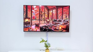 A white desk with a flat-screen TV mounted above it, displaying a vibrant autumn scene.