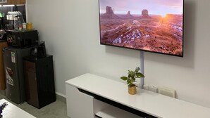 A modern living room with a flat-screen TV mounted on the wall, a white entertainment unit below, and a wooden cabinet to the left.
