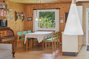 Una habitación con paneles de madera, una mesa de comedor, sillas, un piano y un gran ventanal con vistas a la vegetación.