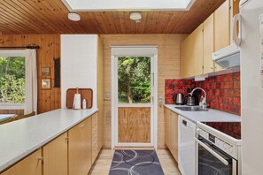 A compact kitchen with wooden cabinets, a built-in oven, and a red backsplash.