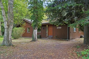 A wooden cabin with a porch, surrounded by trees and a leaf-covered ground.