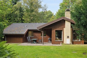 Una cabaña de madera con techo de tejas, una chimenea y un patio con mobiliario exterior.