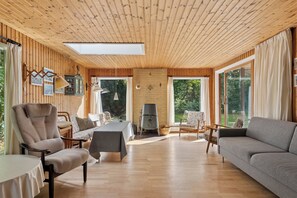 Amplia habitación con paredes de madera, un ventanal grande, un sofá, una silla, una mesa y una chimenea.