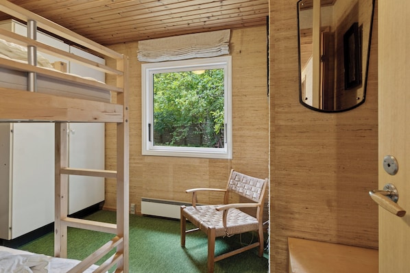 Una habitación con literas, una silla, un ventanal con vistas a follaje y un espejo.