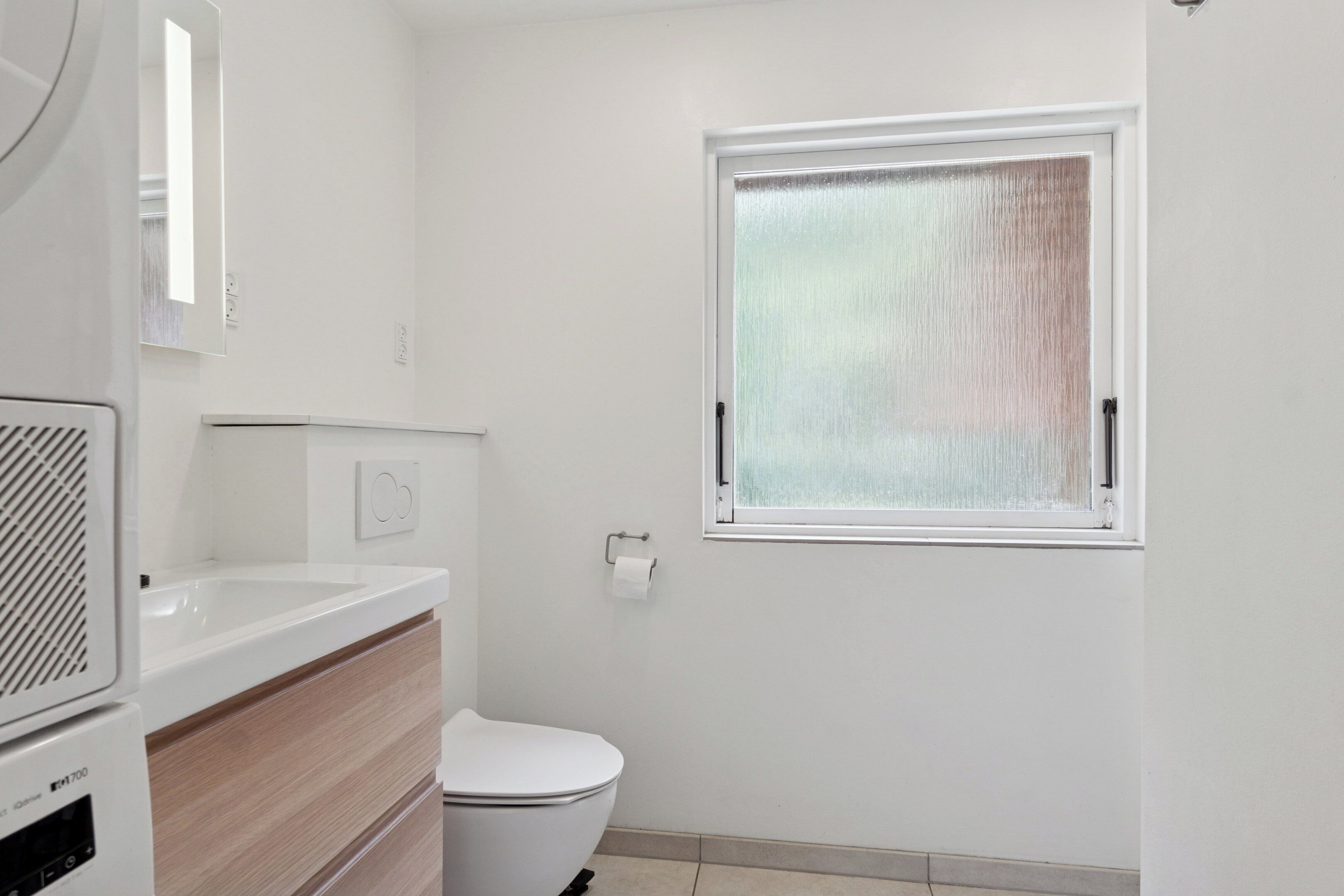 Een badkamer met toilet, wastafel, spiegel en raam.