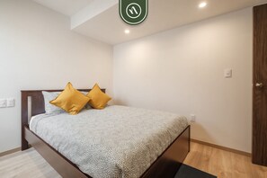 Ein Schlafzimmer mit einem Bett, zwei Kissen, einem Holz-Kopfteil, einer Holztür und einem Lichtschalter an der Wand.