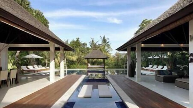 A pool area with lounge chairs and umbrellas, surrounded by wooden decking and palm trees. - Villa Asante | 4BR Family Villa Near Echo Beach | Pool, Chef (Canggu)