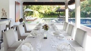 A long dining table set for a meal with white tablecloths, plates, and glasses. - Villa Asante | 4BR Family Villa Near Echo Beach | Pool, Chef (Canggu)