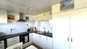 A modern kitchen with white cabinets, a black countertop, and a stainless steel sink. There is a painting above the sink and a poster on the wall. - Chalet Perran Sands, Haven Holiday Park (Perranporth)