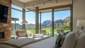 Un dormitorio con una cama grande, un televisor montado en una pared de piedra y un balcón con vistas a formaciones rocosas rojas.