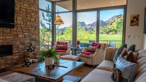 Amplia sala de estar con un ventanal que ofrece vistas a un paisaje montañoso. Hay una chimenea, un conjunto de sofás y una mesa de centro con objetos decorativos.