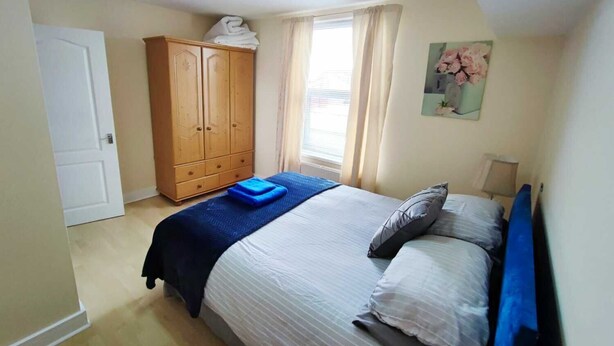 Een slaapkamer met een bed, een kledingkast, een raam met gordijnen en een schilderij aan de muur.