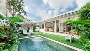 Ein Pool mit Liegestühlen, eine überdachte Terrasse und üppiges Grün.