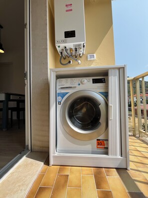 Un lave-linge à chargement frontal doté d’un panneau de commande, situé sur un balcon dont le sol est carrelé.