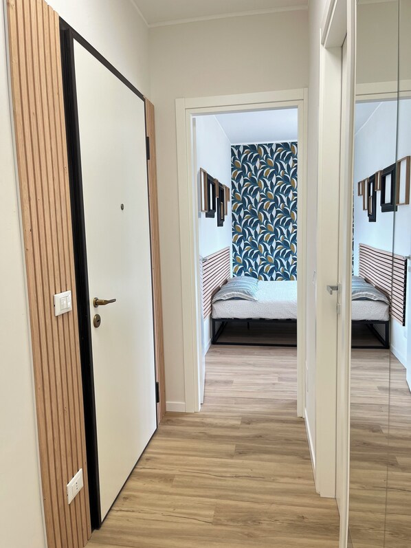 Un couloir menant à une chambre à coucher, avec un lit, un mur orné de tableaux encadrés et une porte en bois.