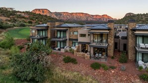 A modern multi-story residential building with large windows and balconies, situated in a hilly area with a view of distant mountains.