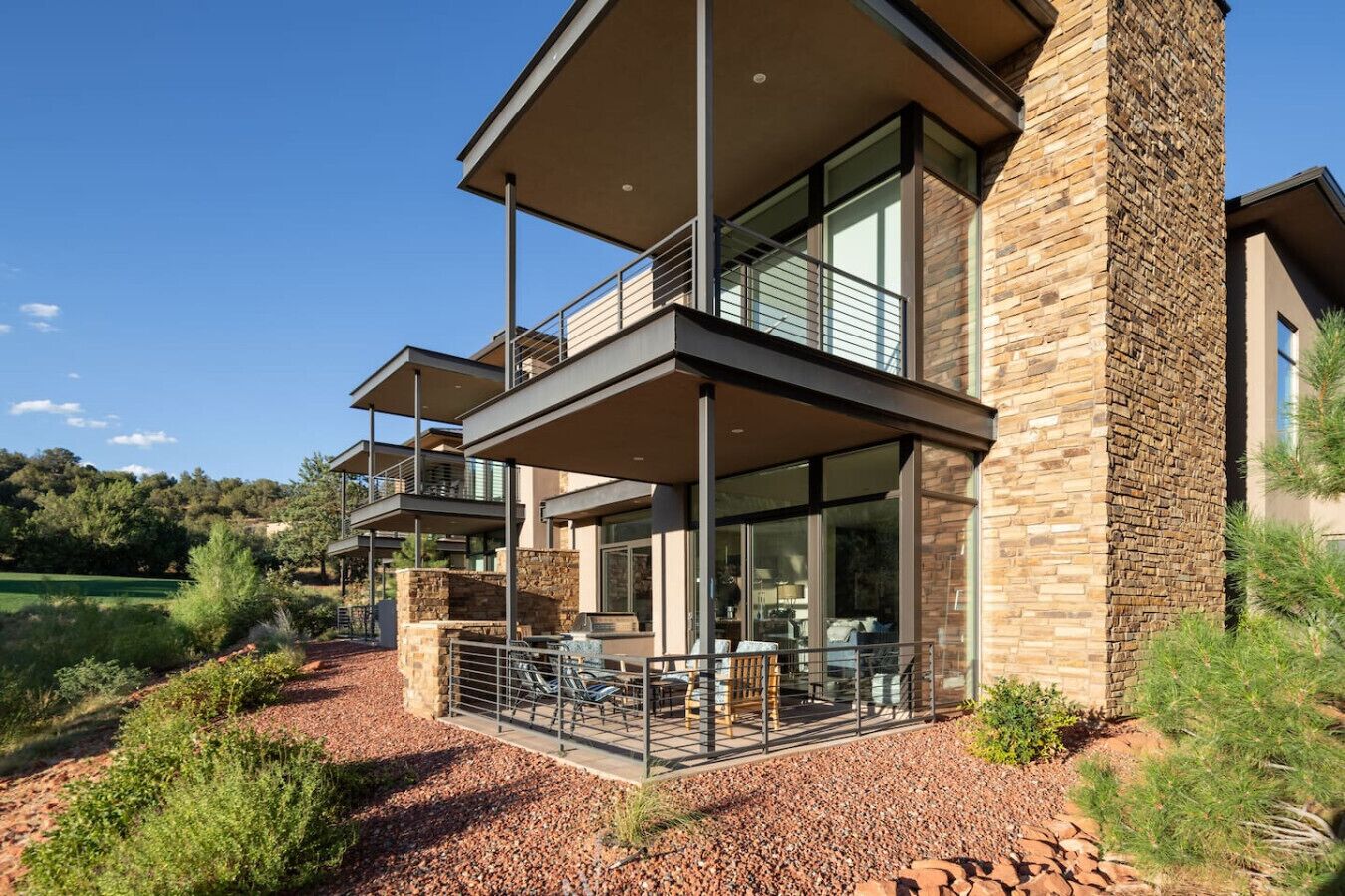 A modern two-story house with a balcony, large windows, and a stone exterior.