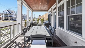 Une terrasse extérieure couverte, dotée d’un plafond en bois, de rampes blanches et de grandes fenêtres.