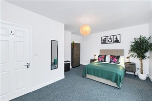 A bedroom with a bed, a nightstand, a lamp, a potted plant, a mirror, and a door.