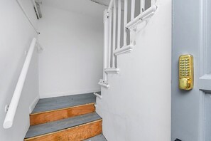 A staircase with wooden steps and white walls, leading to a door with a gold security keypad.