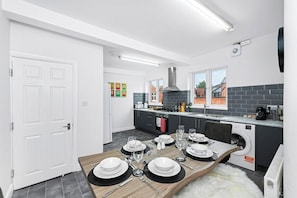 A modern kitchen with a dining area set for six, a washing machine, and a large window.
