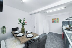 A modern kitchen with a dining area, white walls, and grey tiles.