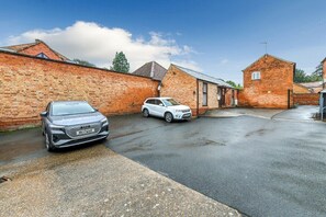 A residential street with two cars parked in a driveway, brick houses, and a clear sky.