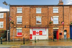 A red brick building with a white signboard, a red door, and a flag.