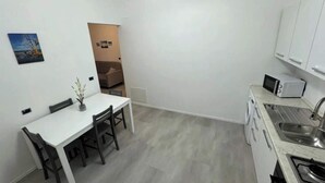 Eine kompakte Küche mit weißen Schränken, einer Mikrowelle, einem Spülbecken und einem Essbereich mit Tisch und Stühlen.