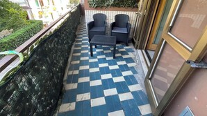 Ein Balkon mit einem Schachbrettmuster-Boden, zwei Korbstühlen und einem kleinen Tisch.