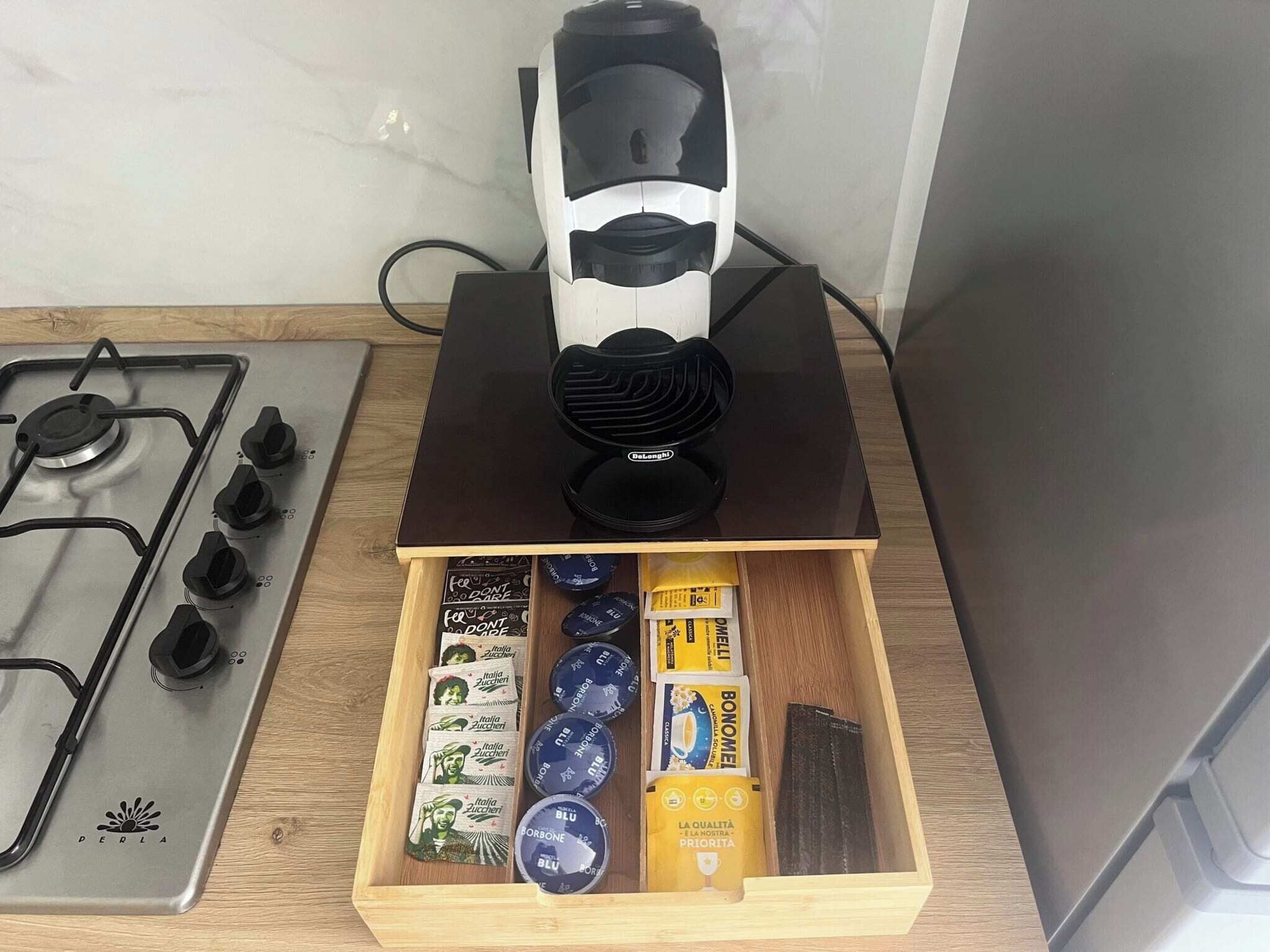 Eine Küche mit Gasherd, einer Kaffeemaschine und einer Schublade mit Kaffeekapseln und einer Schachtel.
