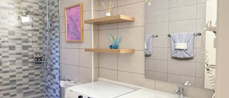 A modern bathroom with a glass shower, a white sink, and wooden shelves.
