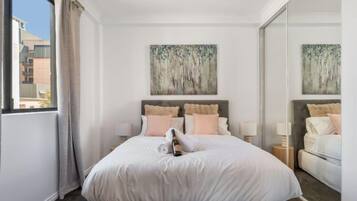 A hotel room with a large bed, two bedside tables, a window with curtains, and two paintings on the wall.