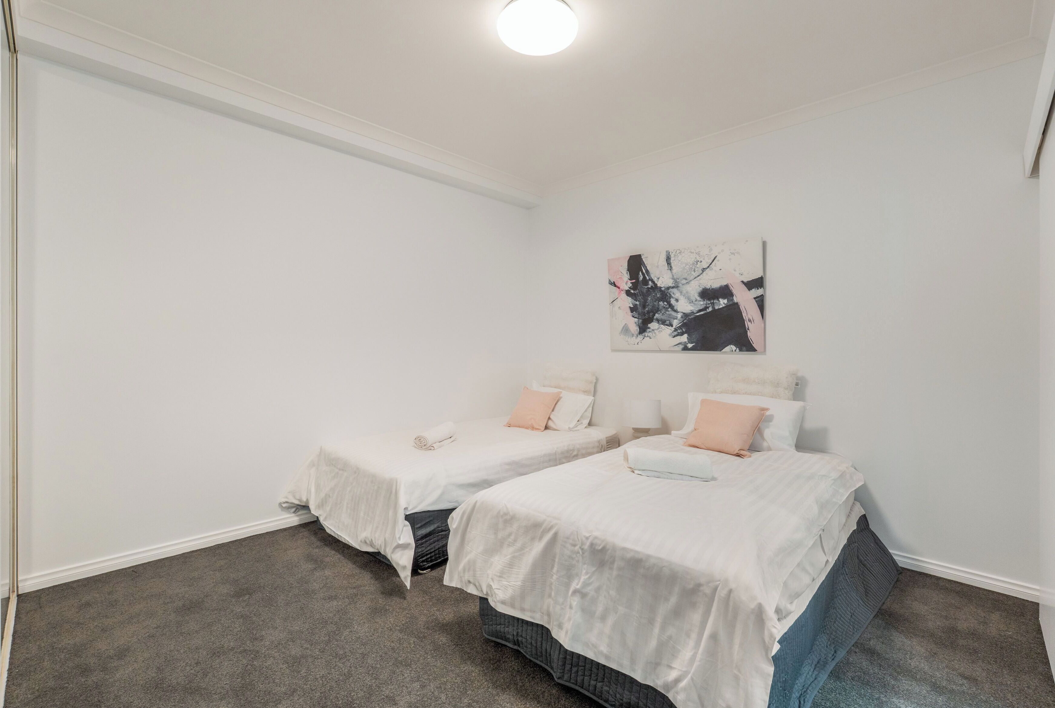 A bedroom with two single beds, a gray carpet, white walls, and a ceiling light.