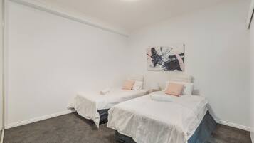 A bedroom with two single beds, a gray carpet, white walls, and a ceiling light.