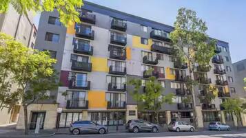 A multi-story residential building with balconies, parked cars, and trees.