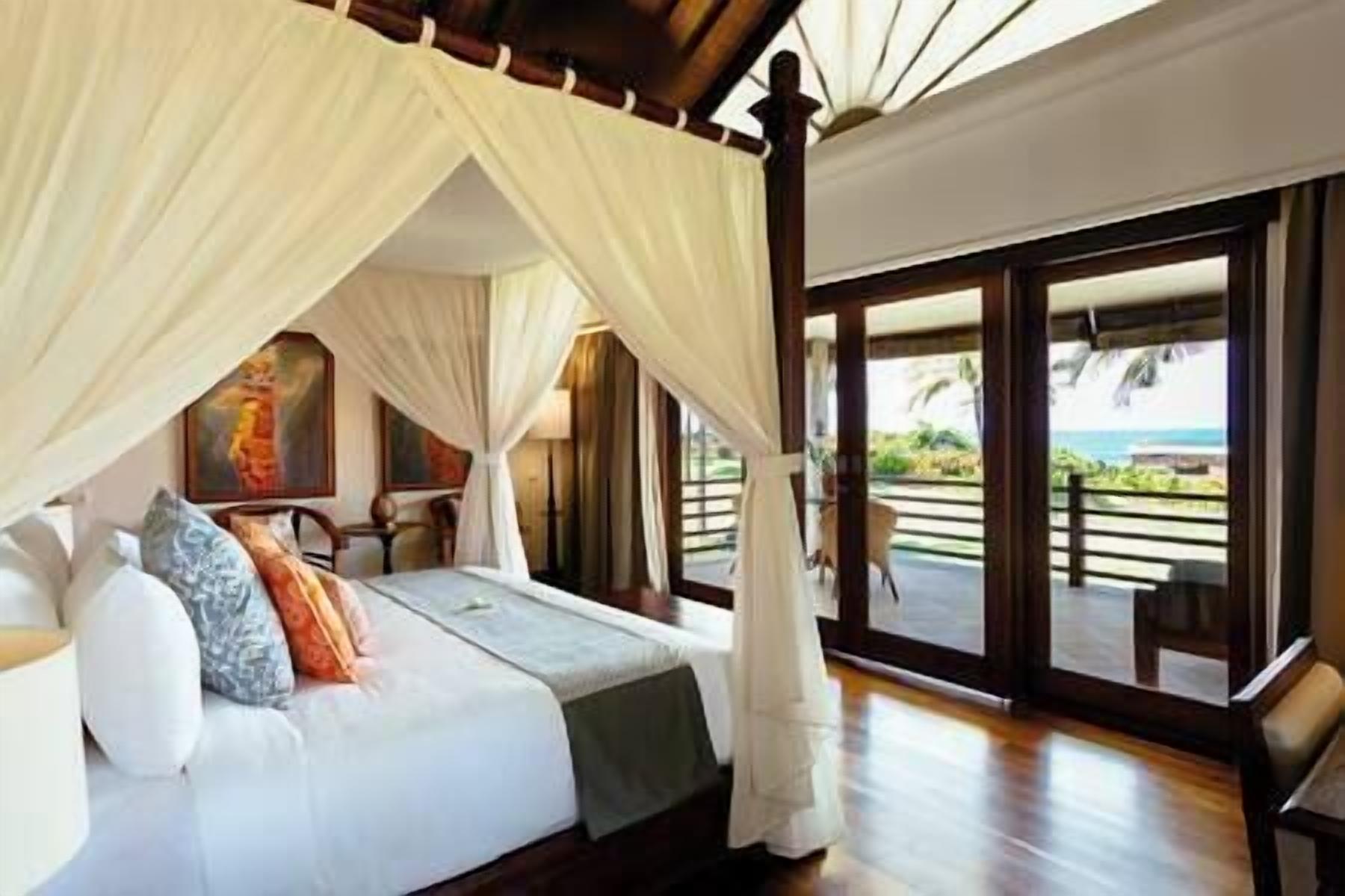 A bedroom with a canopy bed, a desk, and a view of the ocean.