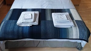 Un lit bien fait, avec une literie à rayures et deux oreillers, flanqué de deux tables de chevet sur lesquelles sont posées des lampes, dans une pièce au plancher en bois.