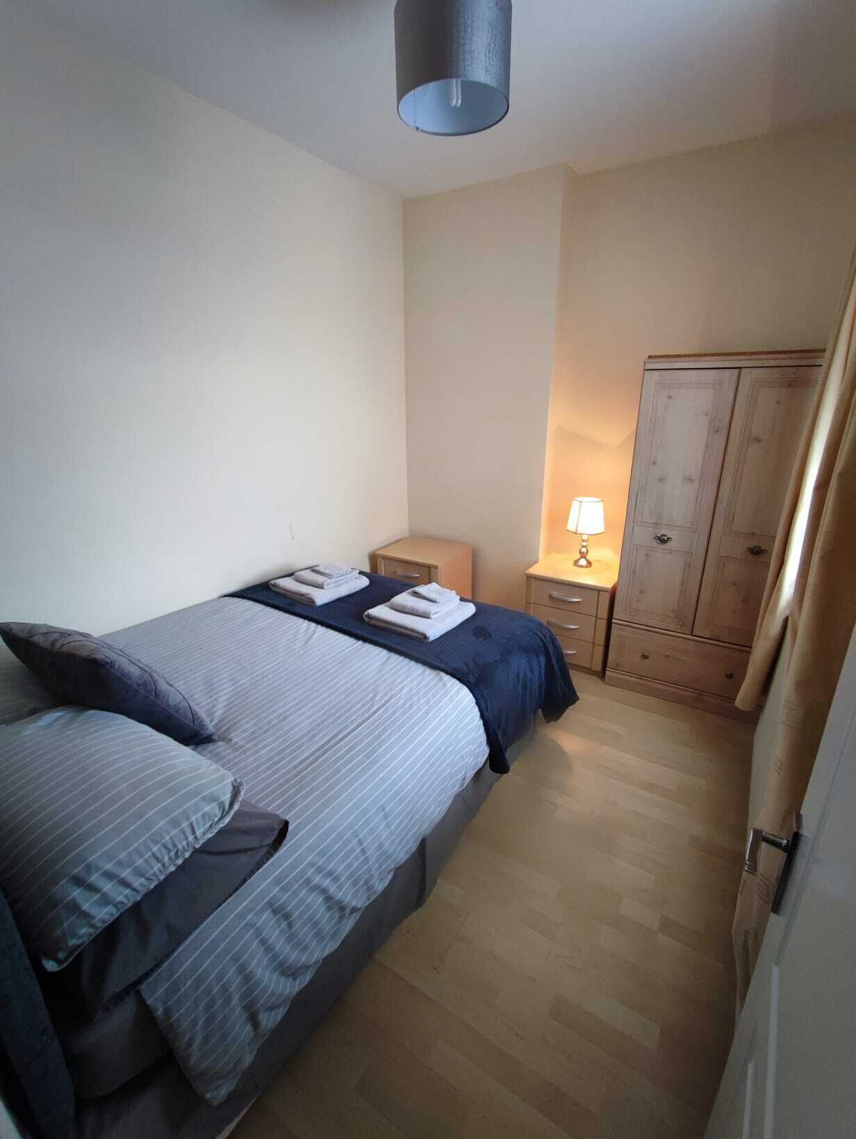 Une chambre à coucher comprenant un lit, une table de chevet, une lampe, une armoire et un luminaire suspendu.