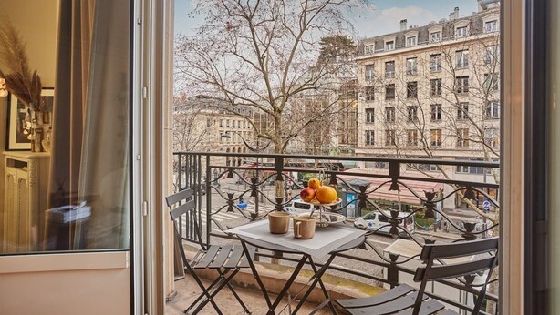 A balcony with a table, chairs, and a fruit bowl.