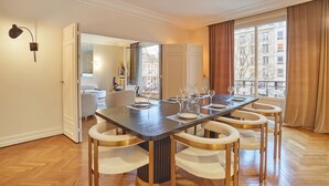 A dining area with a long table, six chairs, and a view of the city through large windows.