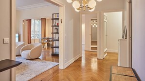 A spacious living area with a modern chandelier, a seating area with a sofa and armchairs, and a wooden floor.